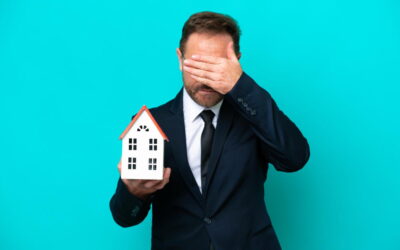 Un homme en costume, l’air inquiet, tenant une petite maquette de maison d'une main et se couvrant le visage de l'autre, illustrant le désarroi lié aux vices cachés et litiges après un achat immobilier.