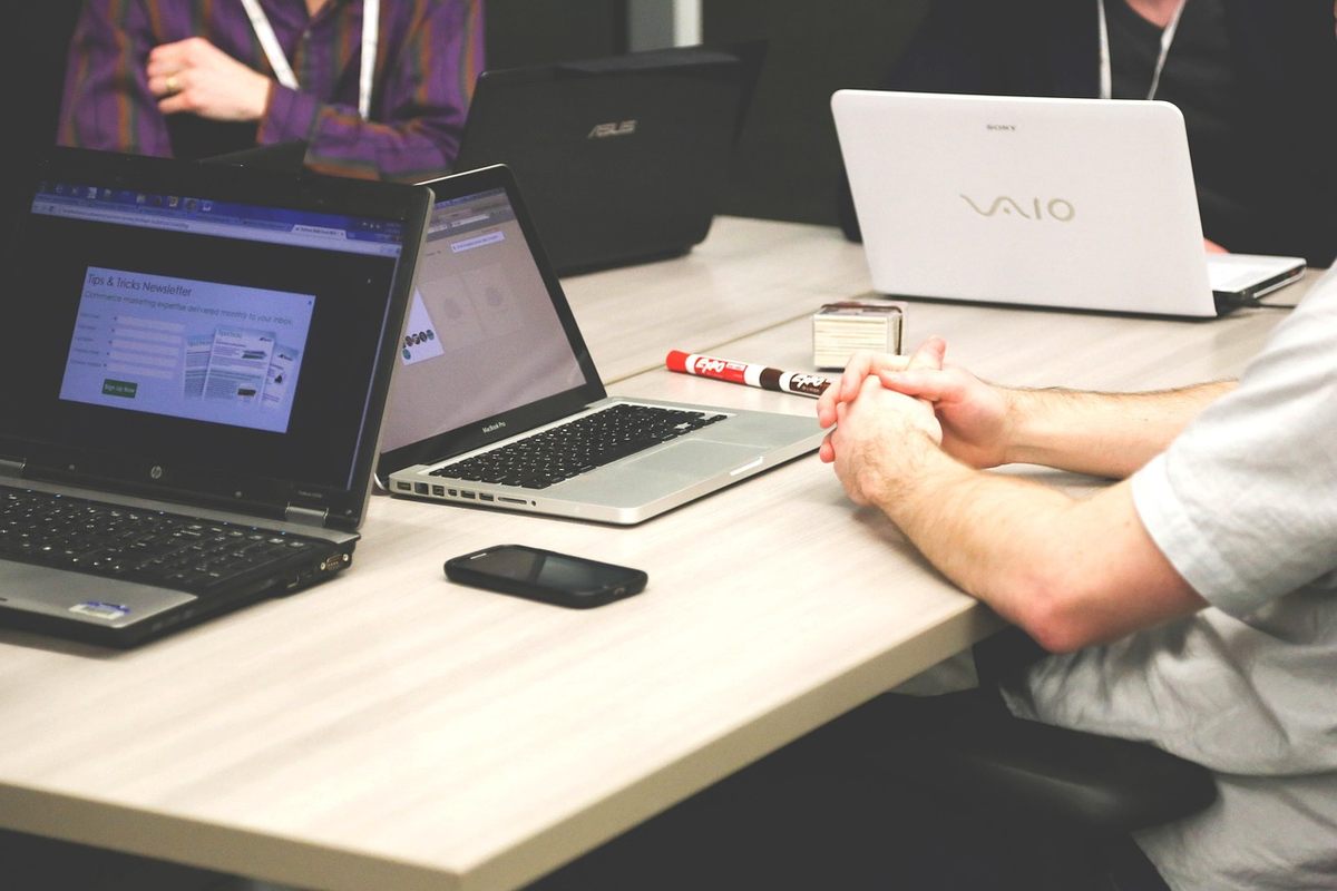 Des personnes discutent autour de laptops et d'un smartphone sur une table Des personnes discutent autour de laptops et d'un smartphone sur une table